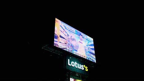 LED-billboard-in-Thailand-zooming-out-revealing-an-active-supermarket-advertisement,-Lotus's,-KFC,-and-MK-restaurant