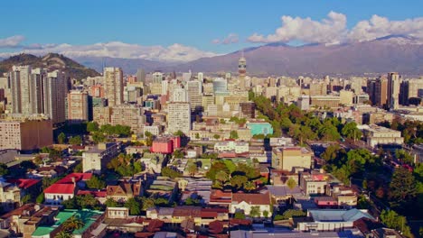 Aerial-truck-right-orbit-of-Santiago-Chile-skyline,-city-center,-Entel-Tower-and-Andes-mountain-range