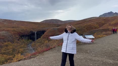 Fröhliche-Blonde-Touristin-Lächelt-Mit-Dem-Svartifoss-Wasserfall-Im-Hintergrund