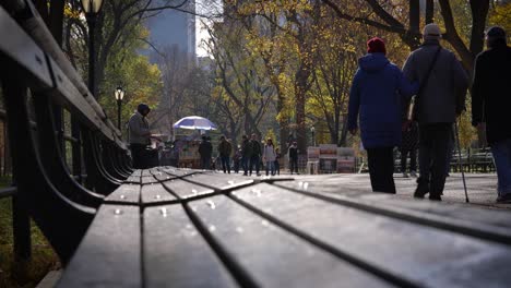 Central-Park,-Park-Bench---A-creative-look-at-Central-Park-from-the-seat-for-a-park-bench,-in-the-fall,-as-people-walk-by