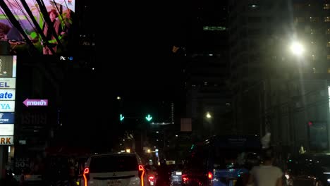 Vehicles-moving-after-the-traffic-light-turned-green-on-the-Ratchada-road-with-billboards-and-buildings,-Bangkok,-Thailand