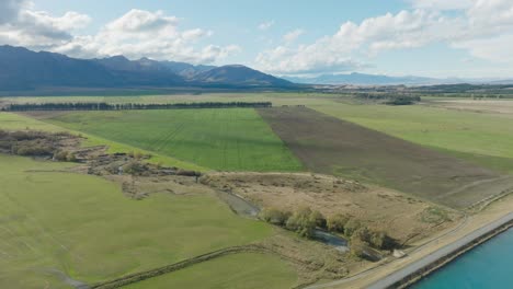 Aerial-view-of-flat-plateau-of-green-agricultural-fields-at-the-base-of-the-Southern-Alps-in-rural-Mackenzie-District,-South-Island-of-New-Zealand-Aotearoa