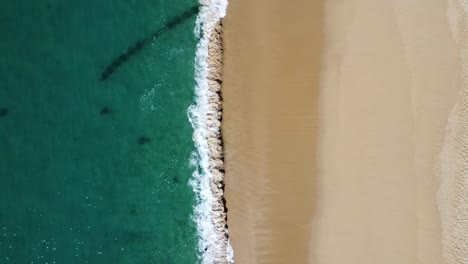 Aerial-top-down-descending-shot-of-waves-reaching-a-peaceful-empty-sandy-beach