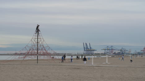 Kids-playing-on-beach-and-climbing-rope-net-Shore-view-with-cranes-Valencia