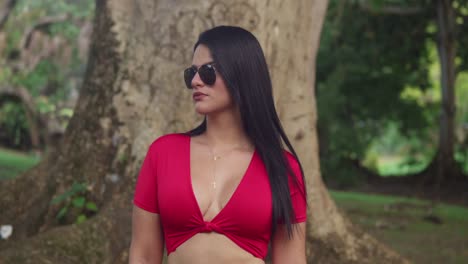 A-stunning-woman-in-a-crimson-dress-walking-graced-a-tropical-park-in-the-Caribbean