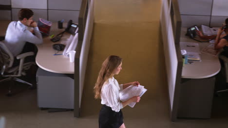 Young-woman-walking-with-paperwork-in-office,-elevated-view