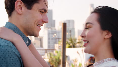 Romantic-Couple-Hugging-On-Rooftop-Terrace-With-City-Skyline-In-Background