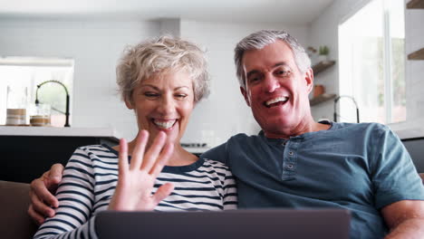 Senior-couple-video-calling-on-a-laptop-waving-at-screen