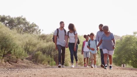 Multi-Generation-Family-Wearing-Backpacks-Hiking-In-Countryside-Together
