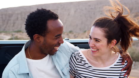 Happy-mixed-race-couple-sitting-on-car-at-roadside,-close-up