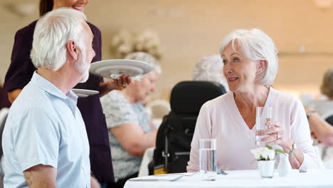 Seniorenpaar-Wird-Von-Betreuer-Im-Speisesaal-Des-Altersheims-Mit-Essen-Bedient