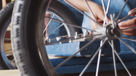Pre-teen-boy-using-a-spanner-to-tighten-a-nut-on-a-bolt,-to-attach-a-wheel-to-his-racing-kart,-close-up,-mid-section-detail,-seen-through-spokes-of-a-wheel