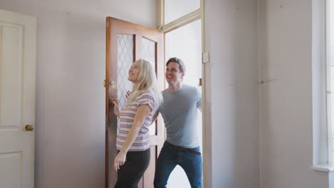 Excited-Young-Couple-Opening-Front-Door-Of-New-Home-And-Hugging-In-Empty-Room