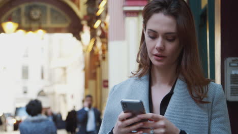 Young-white-businesswoman-standing-on-a-busy-London-street-using-her-smartphone,-close-up,-selective-focus