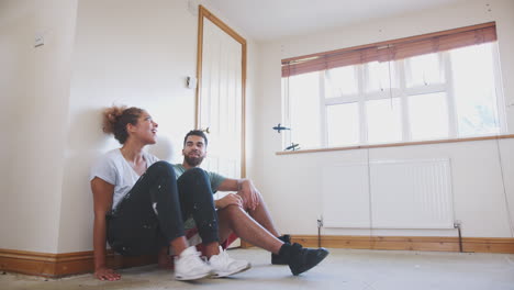 Couple-Sitting-On-Floor-In-Empty-Room-Of-New-Home-Planning-Design
