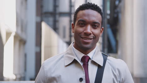 Confident-young-black-businessman-standing-on-the-street-and-smiling-to-camera,-focus-on-foreground,-close-up