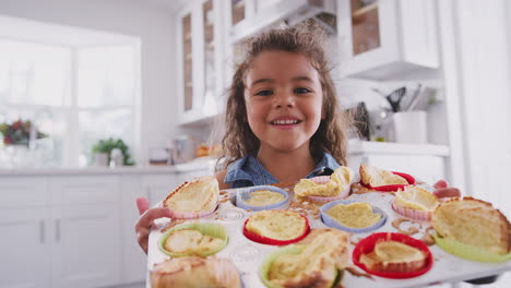 Happy-young-Hispanic-girl-standing-in-kitchen-presenting-the-cakes-she’s-made-to-camera,-close-up