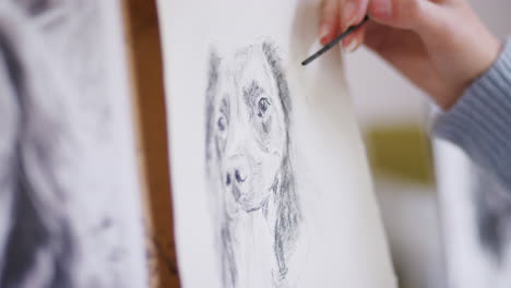 Close-Up-Of-Artist-Sitting-At-Easel-Drawing-And-Smudging-Picture-Of-Dog-Using-Charcoal