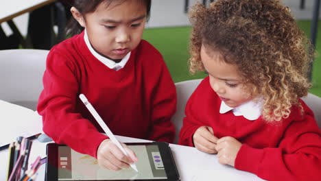 Young-mixed-race-schoolgirls-in-an-infant-school-classroom-drawing-using-a-tablet-computer,-close-up