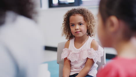 Young-mixed-race-schoolgirl-sitting-in-class-listening-to-story-with-her-classmates,-selective-focus