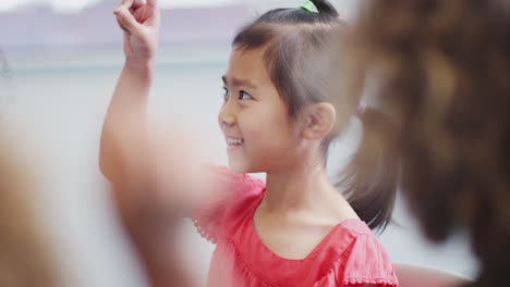 Asian-schoolgirl-sitting-with-her-classmates-in-infant-school-class,-selective-focus
