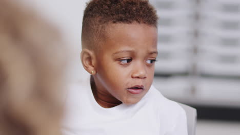 Close-up-of-mixed-race-schoolboy-talking-in-the-classroom-at-infant-school