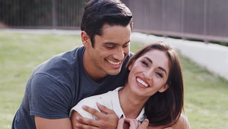 Millennial-Hispanic-couple-embracing-in-the-park-and-smiling-to-camera,-close-up