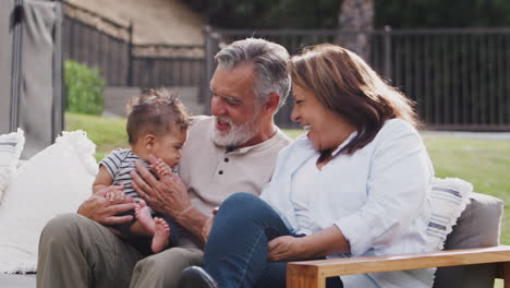 Senior-Hispanic-couple-sitting-on-a-seat-in-the-garden-with-their-baby-grandson,-close-up