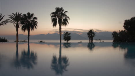 Timelapse-of-evening-on-resort-Pool-palms-and-scene-with-sea-and-mountains