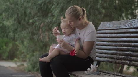 Mum-giving-yogurt-to-baby-daughter-in-the-park