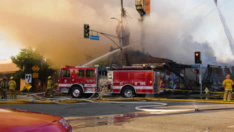 Firetruck-and-firemen-extiguishing-a-burning-building,-sunny-day-in-Los-Angeles