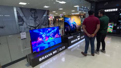 POV-Aufnahme,-Chroma-Showroom-Im-Einkaufszentrum,-Zwei-Männer,-Die-Sich-Die-Leistung-Eines-Sony-Brvia-XR-OLED-Fernsehers-Ansehen-Und-Einkaufen