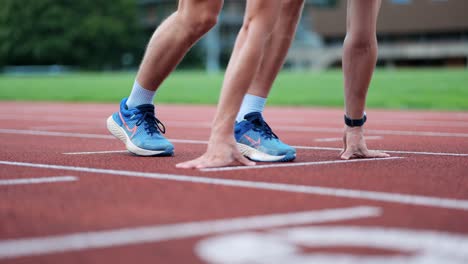 El-Corredor-Masculino-Toma-La-Posición-Inicial-En-El-Marcador-De-La-Pista-De-Atletismo,-Cerca-De-Las-Manos-Y-Los-Pies-Del-Atleta.