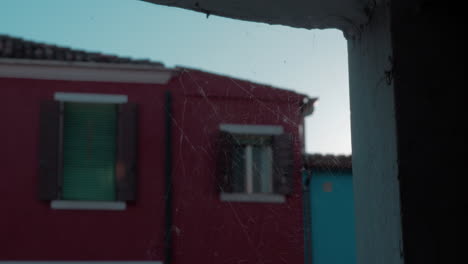 Un-Primer-Plano-De-Una-Telaraña-En-Una-Abertura-De-Piedra-Frente-A-Una-Fachada-De-Burano-Borrosa