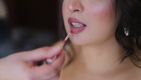 Una-Novia-Se-Prepara-Para-El-Día-De-Su-Boda-Con-La-Ayuda-De-Su-Maquilladora,-Poniéndose-Lápiz-Labial