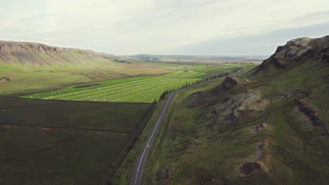 Aerial-car-driving-on-ring-road-Iceland,-nature-grassy-fields-mountain-landscape-golden-hour-warm-sunset