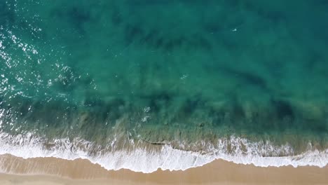 Aerial-top-down-descending-view-over-waves-reaching-an-empty-beach