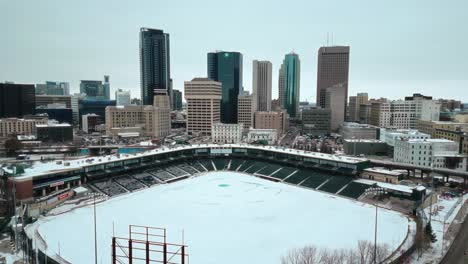 Eine-Umgekehrte-4K-Aufnahme-Einer-Filmischen-Drohnenaufnahme-Von-Wolkenkratzern-In-Der-Innenstadt,-Gebäuden,-Arena-Shaw-Park,-Baseball-Diamant,-Stadtlandschaft,-Winter-In-Der-Hauptstadt-Winnipeg,-Manitoba,-Kanada