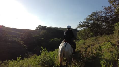Adult-male-practicing-a-horseback-riding-tour-uphill-in-the-tropical-forests-of-Monteverde,-Costa-Rica,-wearing-protection-gear-and-a-backpack