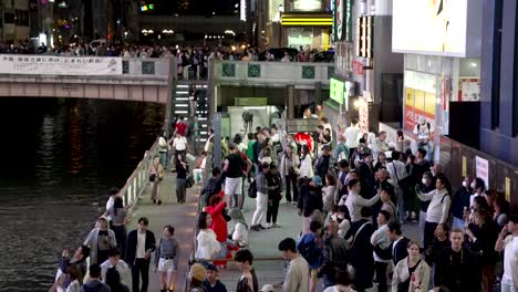 Geschäftige-Menschenmengen,-Die-Von-Neon-Plakatwandlicht-Beleuchtet-Werden-Und-Nachts-Fotos-Von-Glico-Mann-Neben-Dem-Dotonbori-Kanal-Machen