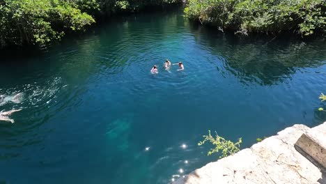 People-swimming-and-enjoying-in-crystal-clear-turquoise-water-Nicte-ha-cenote-in-Tulum,-Mexico