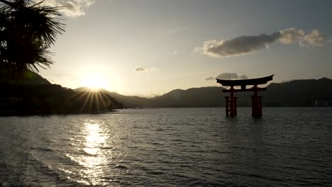 Silhouette-Des-Schwimmenden-Grand-Torii-Tors-Von-Itsukushima-Mit-Fackeln-Des-Sonnenuntergangs-Im-Hintergrund