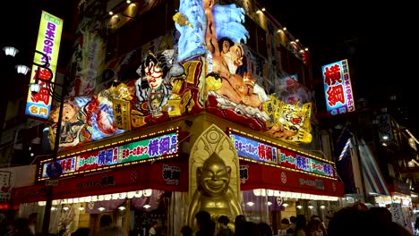 Illuminated-Colourful-Display-Above-Restaurant-With-Biliken-Statue-On-Corner-In-Shinsekai-Area-At-Night
