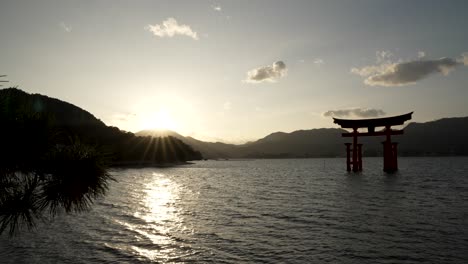 Die-Silhouette-Von-Itsukushima-Jinja-Otorii,-Die-Während-Des-Sonnenuntergangs-Schwebt,-Flackert-Im-Hintergrund-Auf