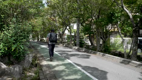 Male-Solo-Traveller-Wearing-Backpack-Walking-uphill-Along-Pedestrian-Path-In-Mitaki,-Japan