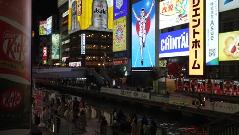 Tourists-Walking-Along-Dotonbori-Canal-With-Neon-Lit-Illuminated-Billboards-In-Osaka-At-Night