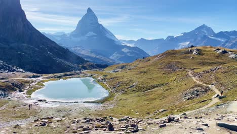 Mountain-Freedom:-Matterhorn-Mountain-Landscape-Near-Rotenboden-and-Gornergart,-Switzerland,-Europe-|-Shaky-Movement-Over-Rough-Landscape-at-Travel-Couple-Explores-Lake-In-Distance,-Hiking