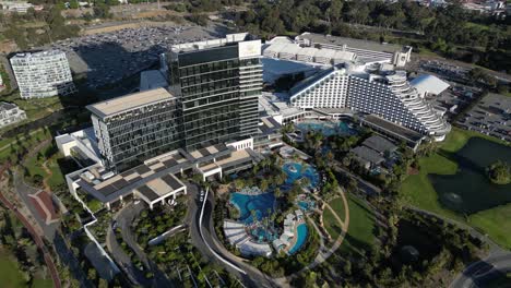 Toma-De-Arriba-Hacia-Abajo-Con-Drones-Del-Hotel-Crown-Casino-En-La-Ciudad-De-Perth-Con-Piscina-Y-Palmeras-En-El-Jardín-Al-Atardecer