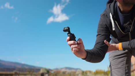 Close-up-of-hand-holding-innovative-DJI-Osmo-Pocket-3-stabilized-handheld-mobile-camera-with-blue-sky-in-background