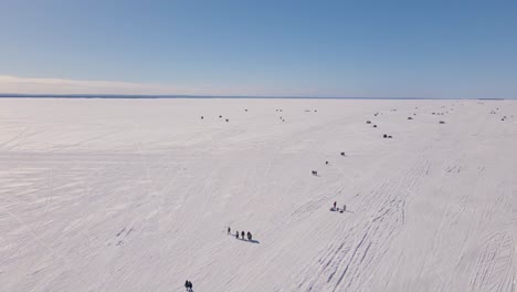 A-wide-angle-drone-shot-following-family-and-friends-walking-on-a-frozen-lake-back-to-shore-after-a-long-day-of-ice-fishing-during-a-beautiful-cold-sunny-winter-day-in-a-remote-part-of-Canada